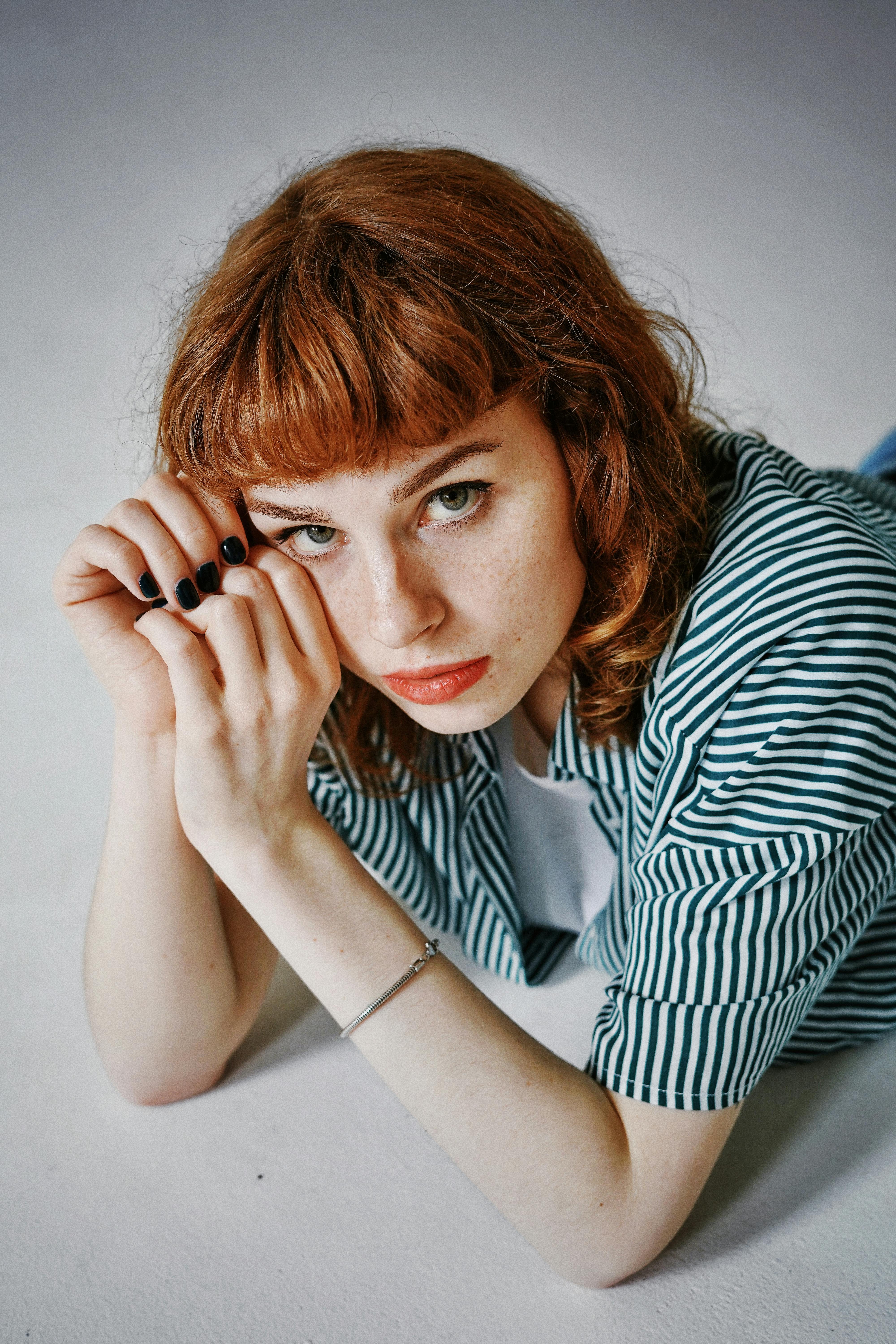 Free A thoughtful portrait of a young woman with red hair lying on a light surface. Stock Photo