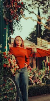 Stylish woman in red sweater amidst flowers at an outdoor market, conveying a vibrant and lively atmosphere.