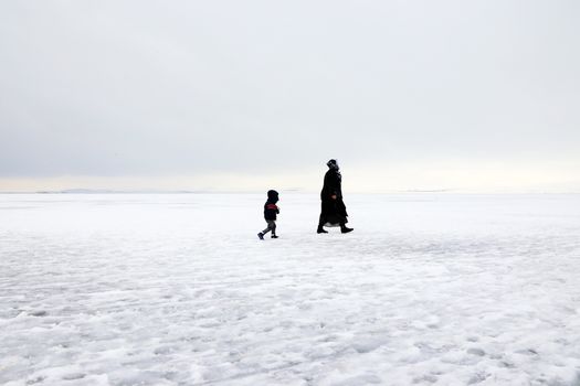 一个孩子和一位成人在寒冷的冬日走过白雪皑皑的广阔地带