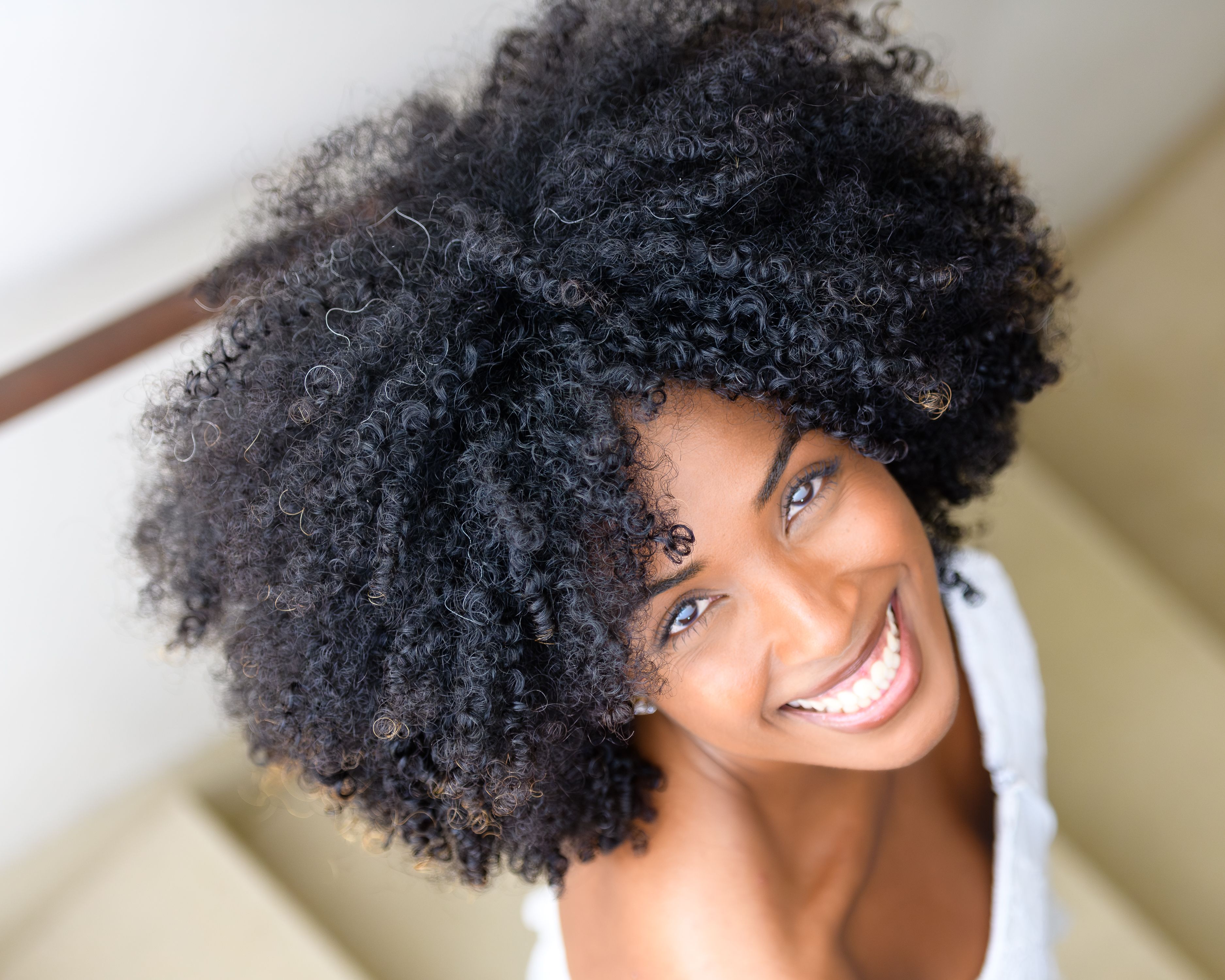 Free Close-up of a smiling woman with curly hair looking up indoors, capturing joy and warmth. Stock Photo