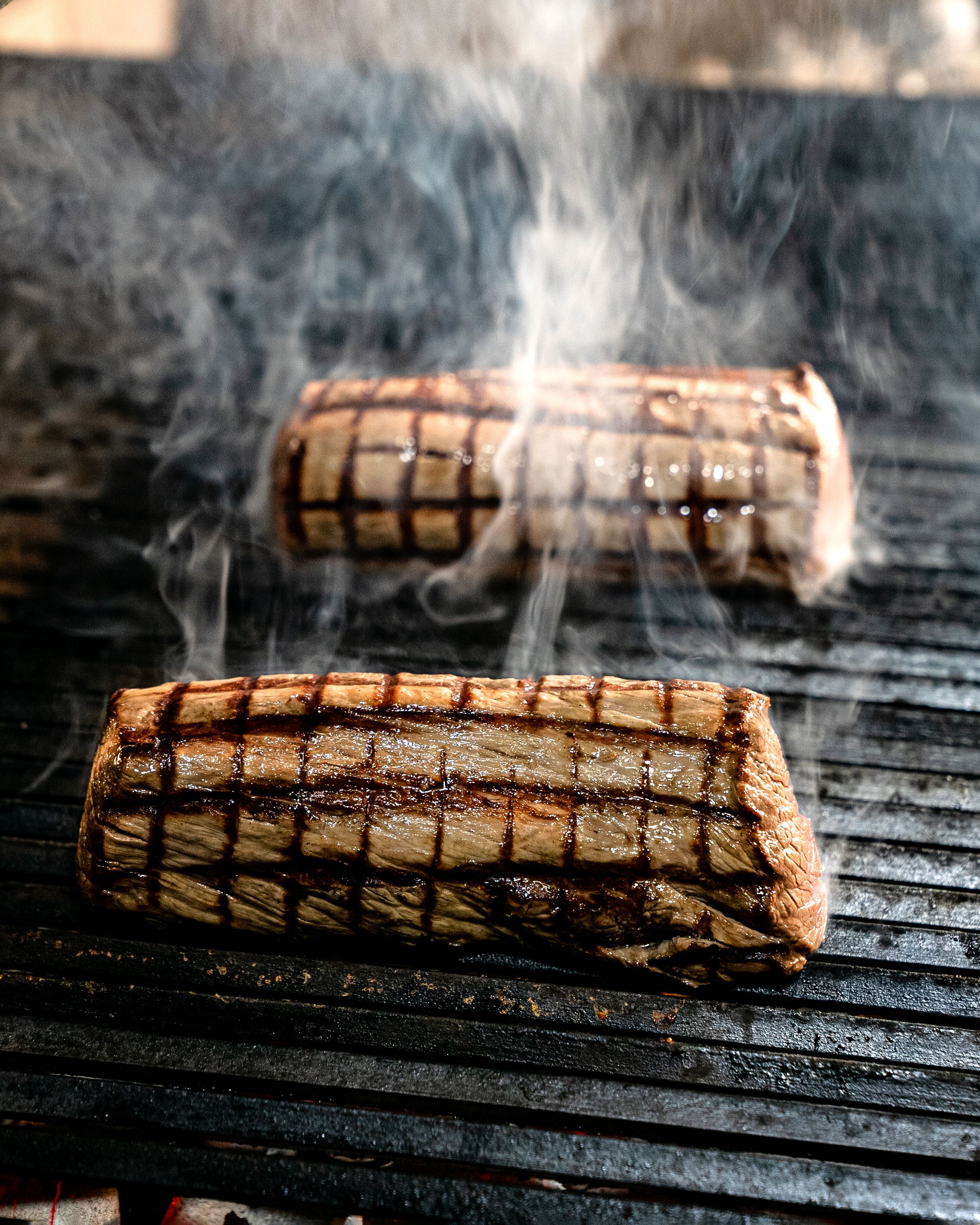 Two delicious steaks with grill marks sizzling with smoke on a barbecue grill.