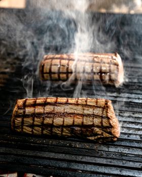 Two delicious steaks with grill marks sizzling with smoke on a barbecue grill.