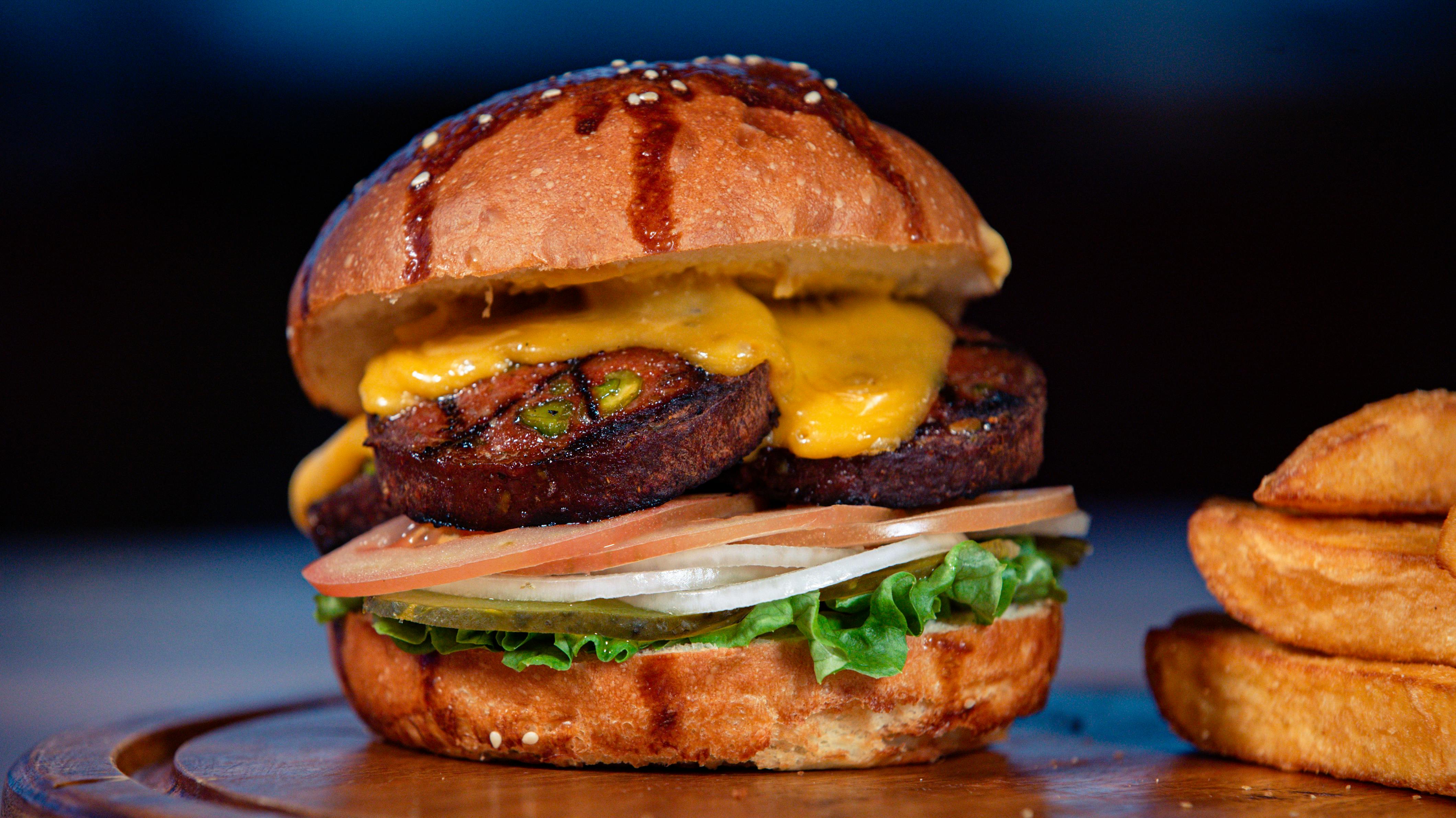 close-up of a loaded veggie burger with sweet potato fries and a side salad