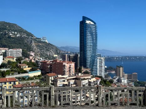 Vibrant view of Monaco's coastline with modern skyscrapers and scenic mountains under a clear blue sky.