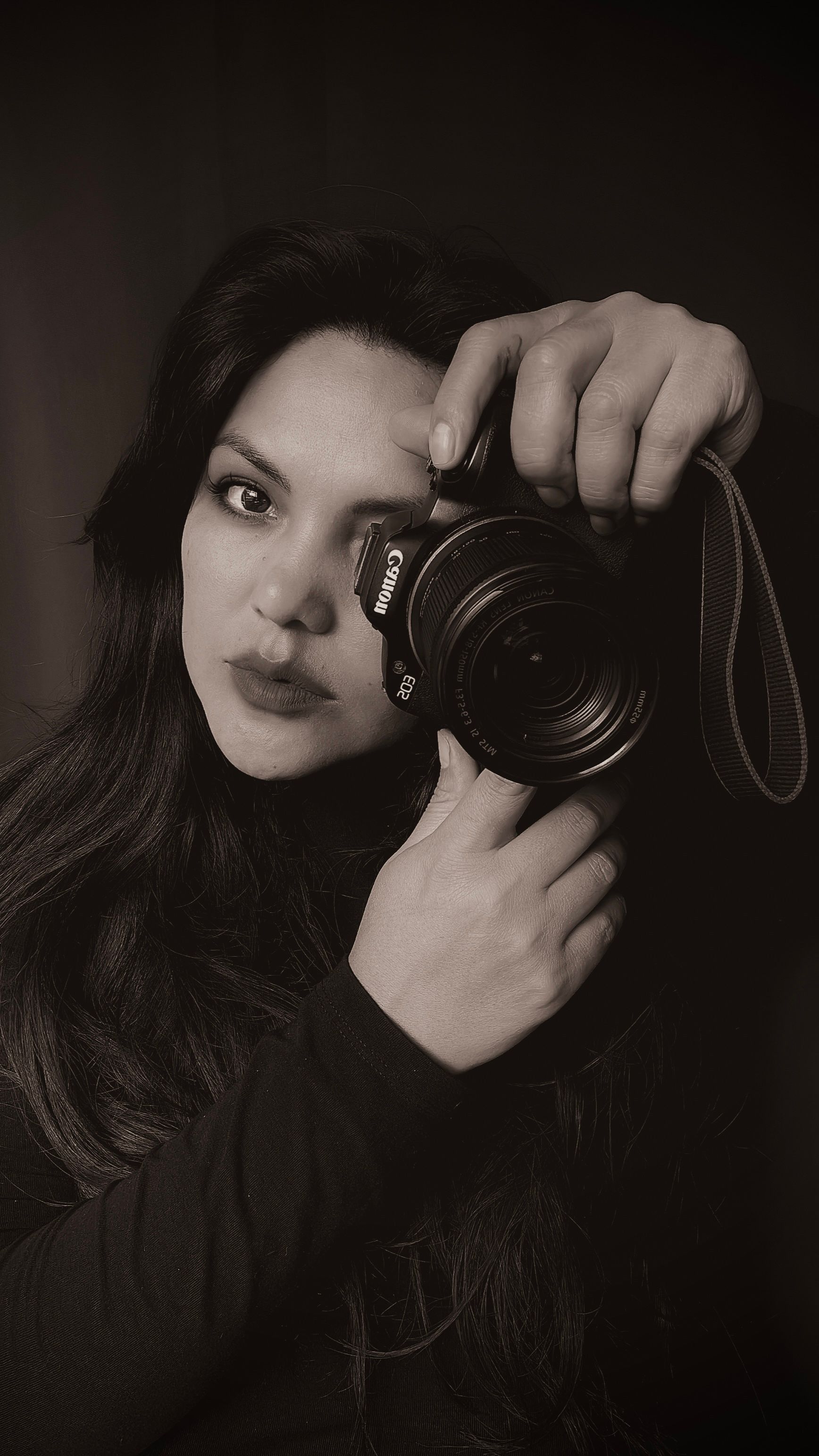 A black and white portrait of a female photographer creatively posing with a camera.