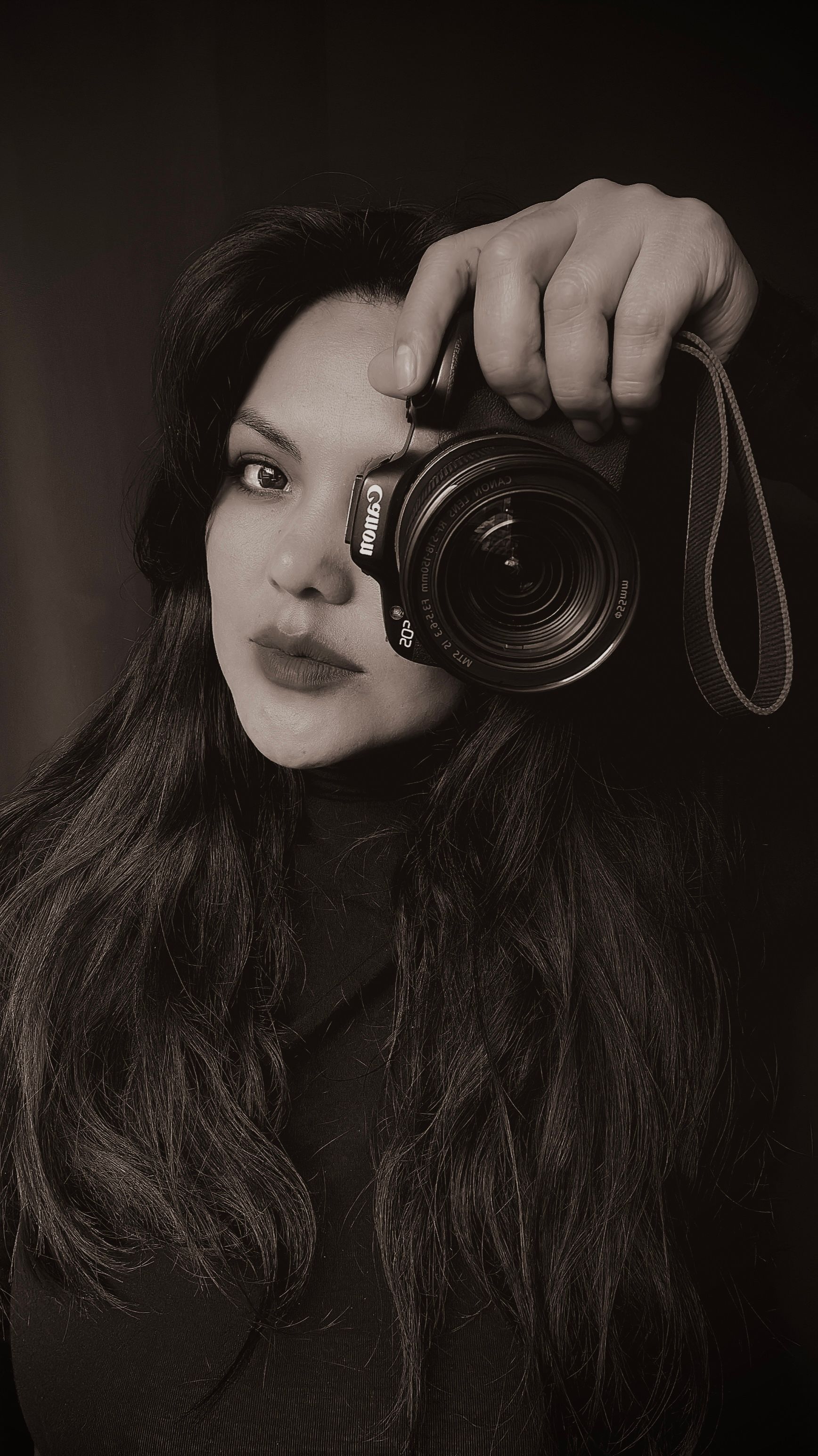 Black and white portrait of a woman holding a camera in front of her face, focused gaze.