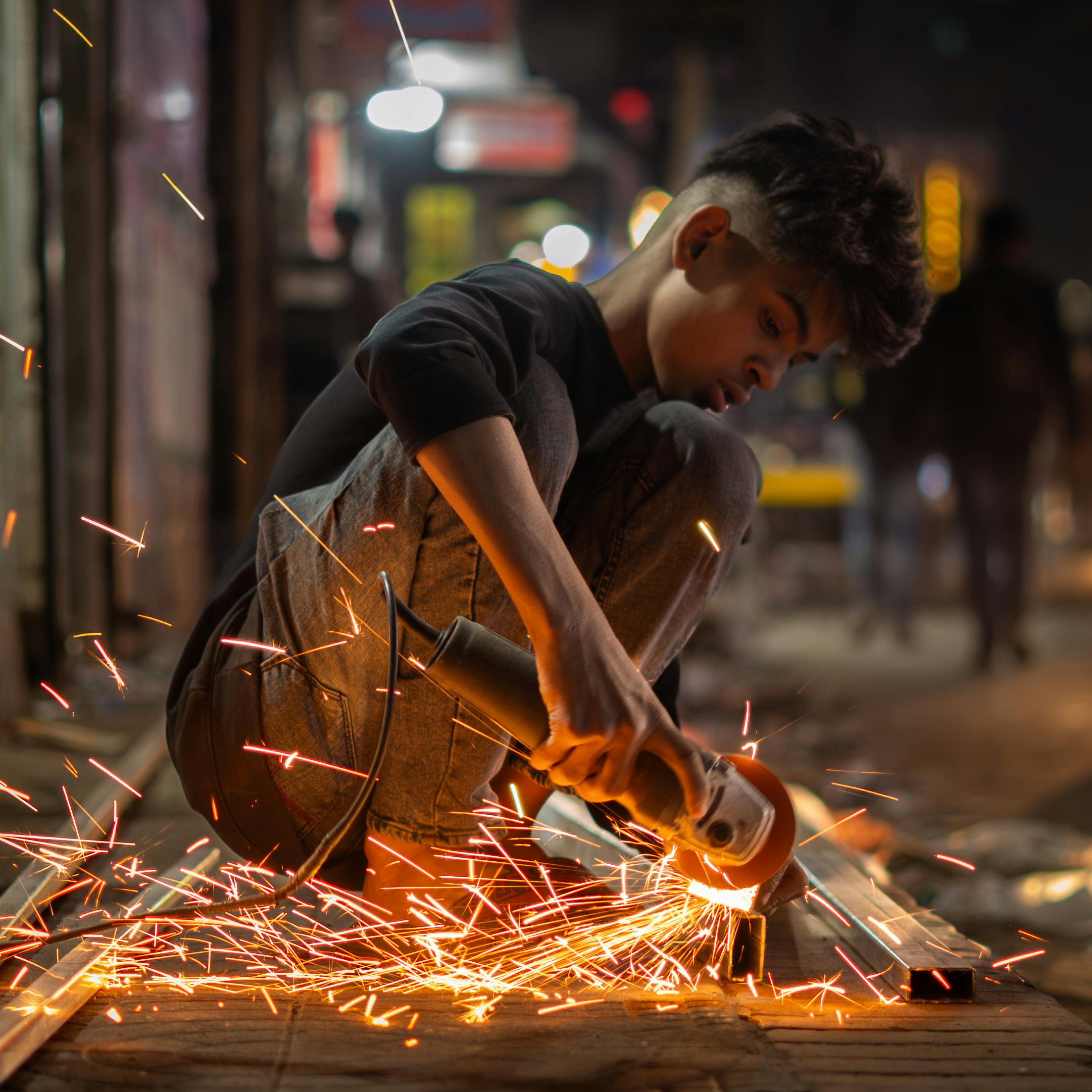 Young male using an angle grinder with sparks flying on a nighttime street.