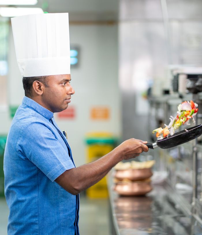 Chef in a blue uniform tossing vegetables in a hot pan in a restaurant kitchen
