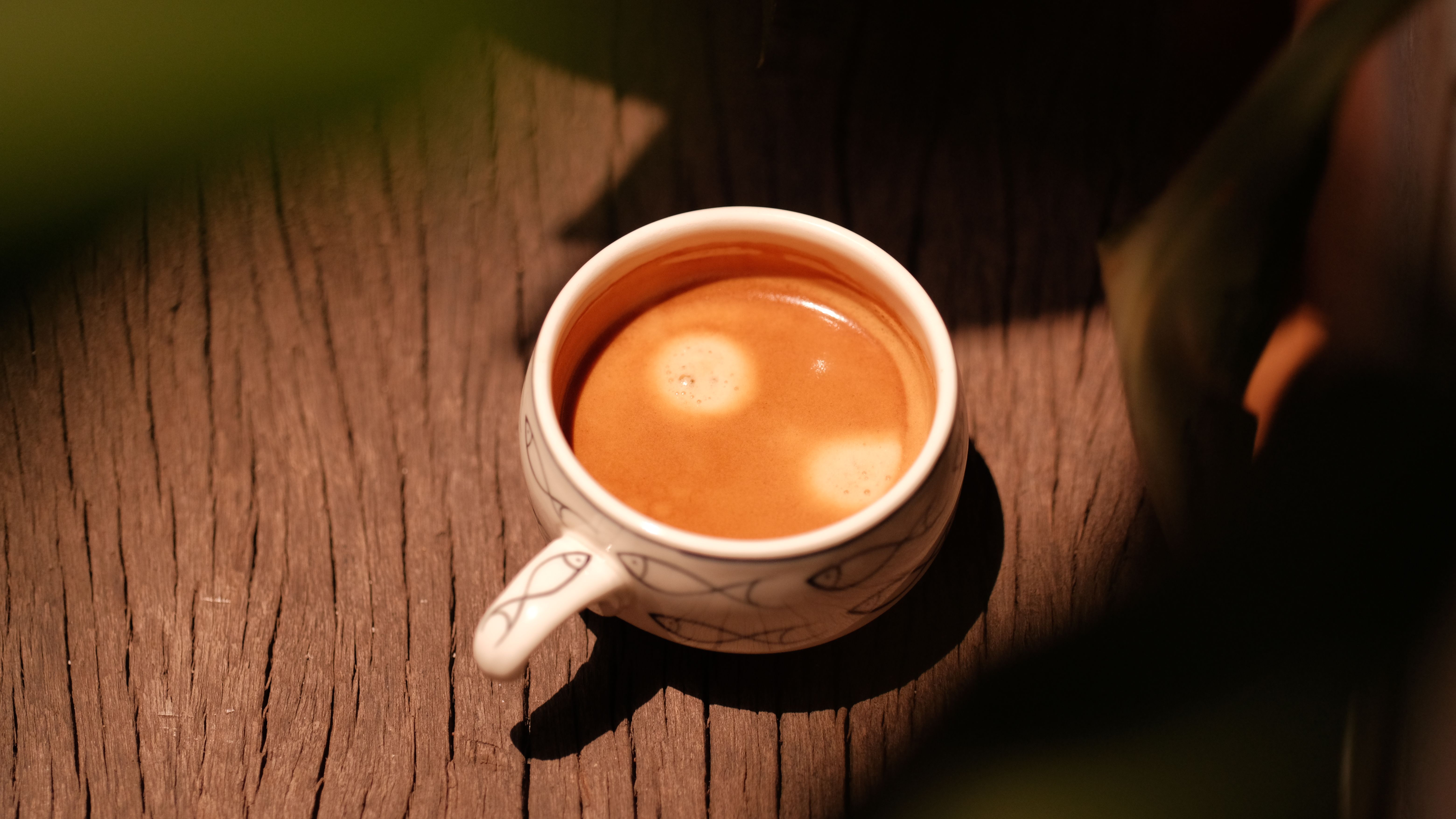 Aerial view of espresso in patterned cup on rustic wooden table, warmly lit.