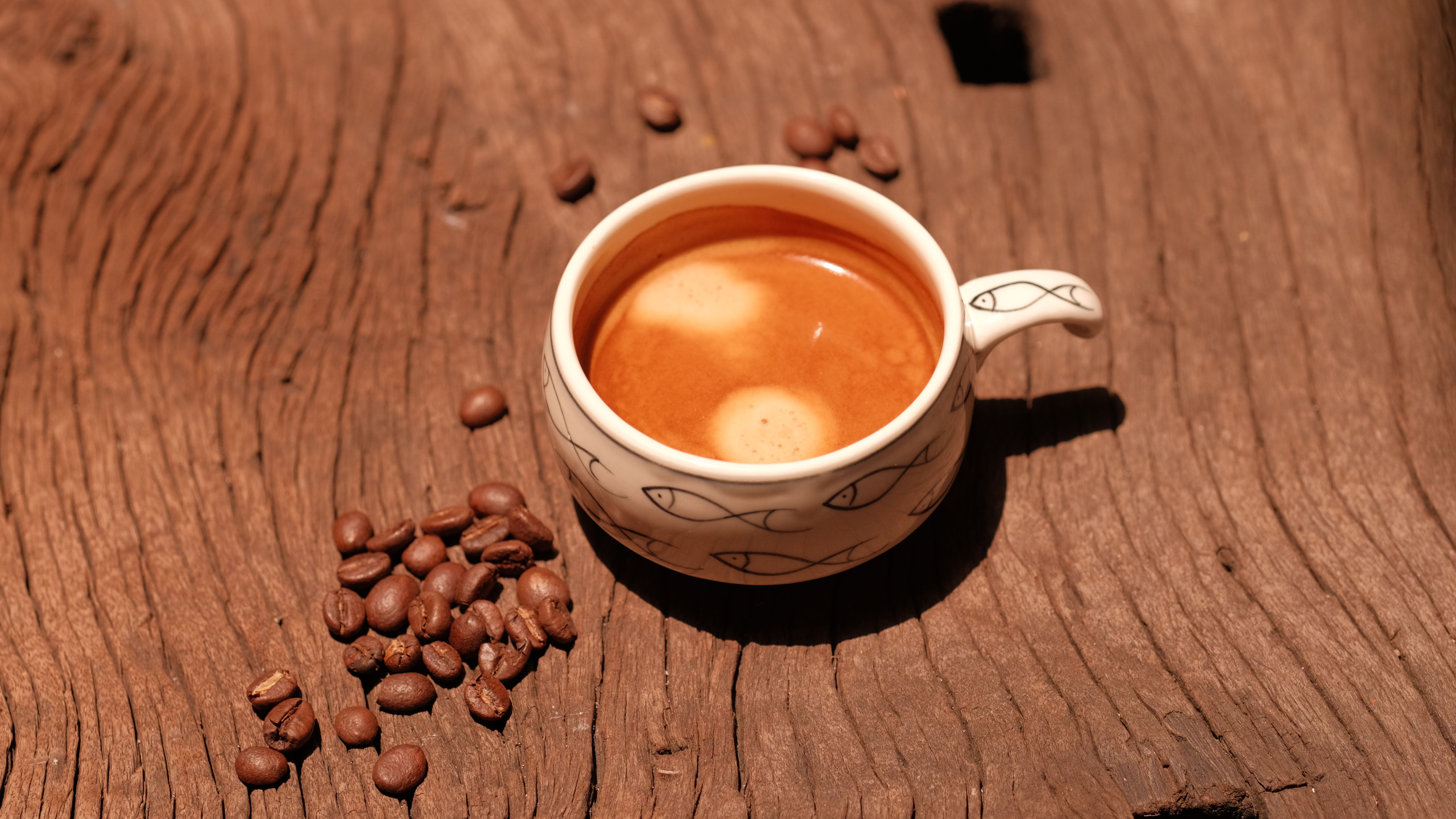 Artistic shot of a coffee cup and beans on a textured wooden surface.