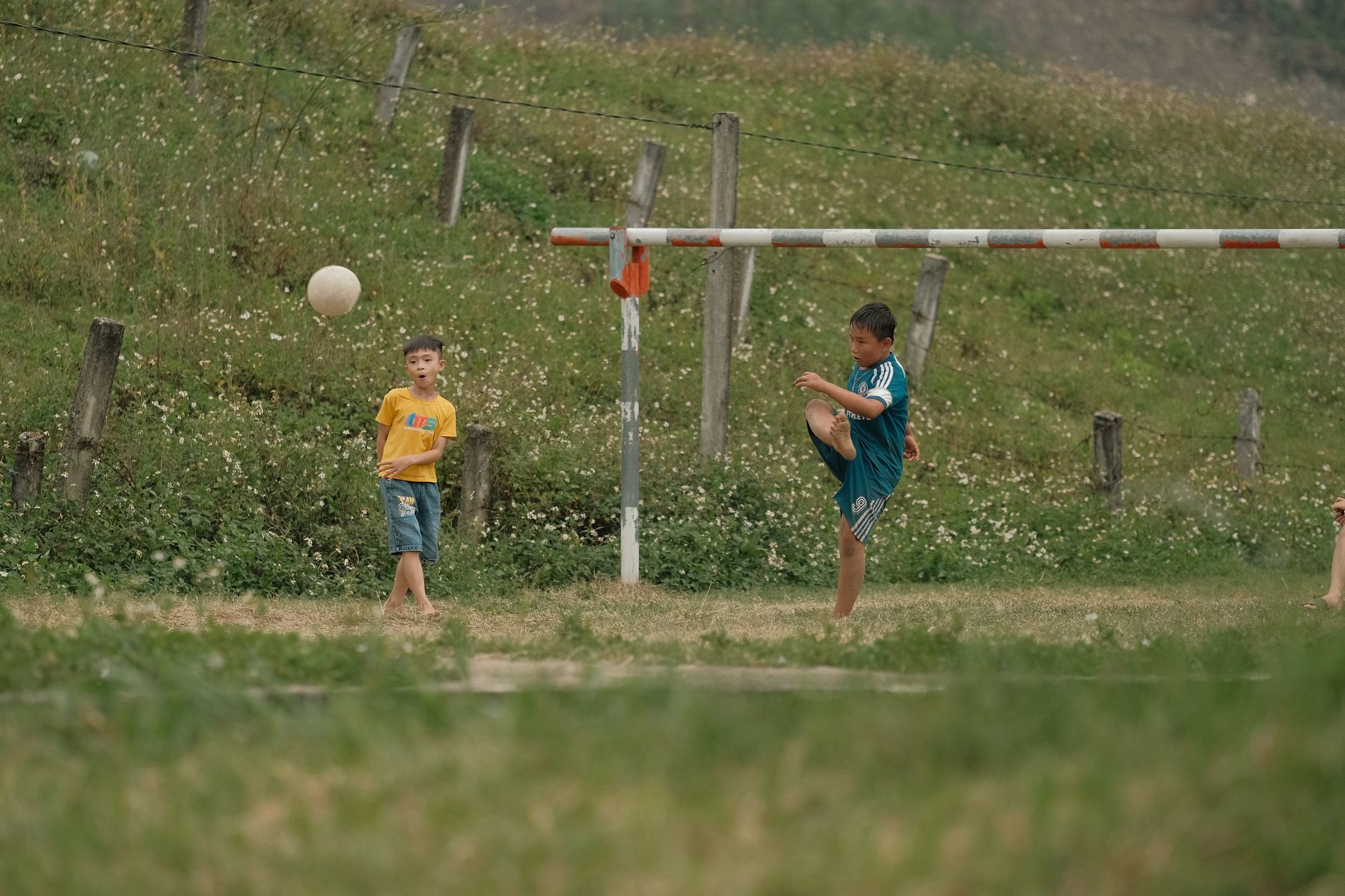 Two children enjoy a soccer game in a grassy outdoor field.