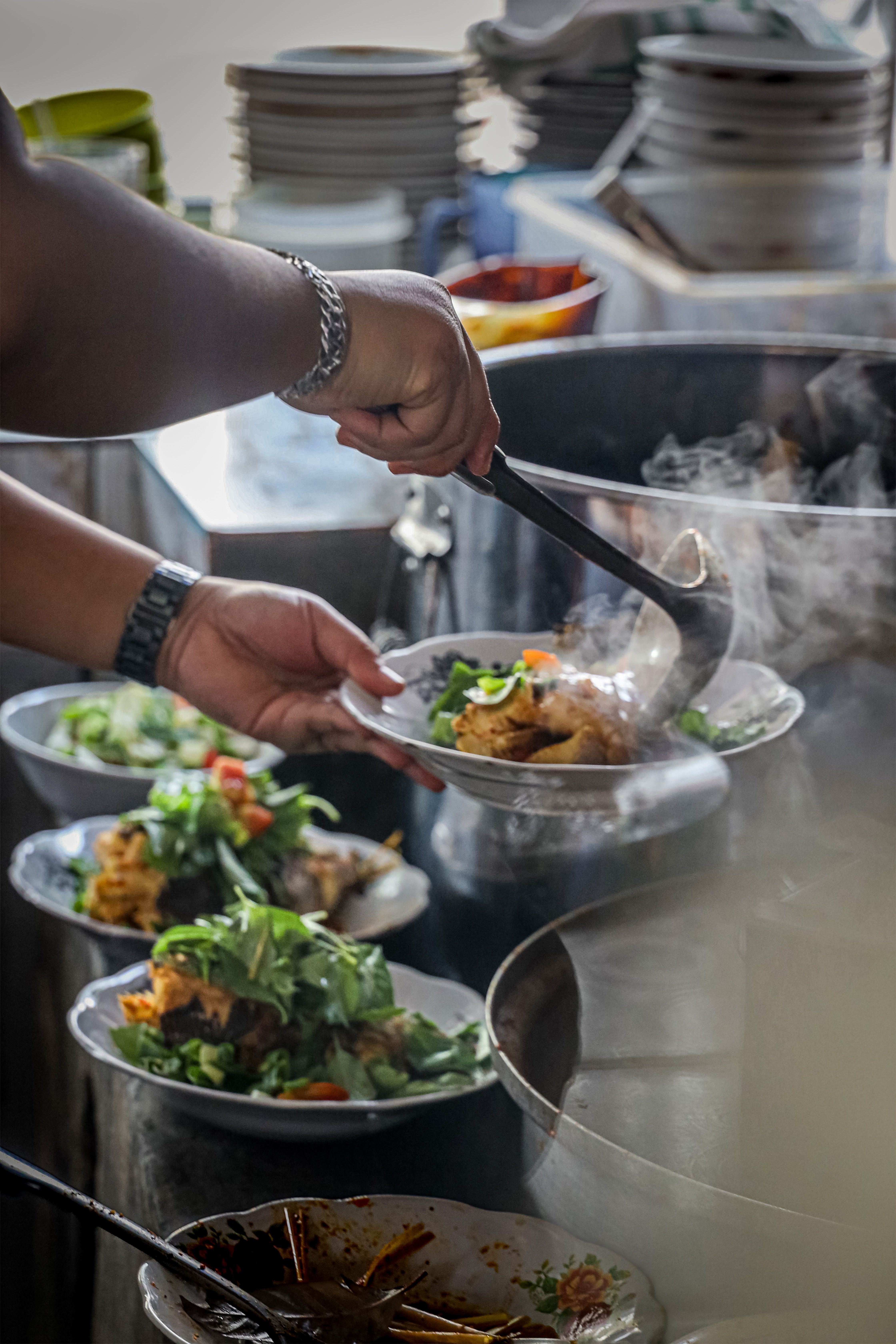 A cook serves traditional Indonesian dishes with steam rising, showcasing vibrant culinary culture.
