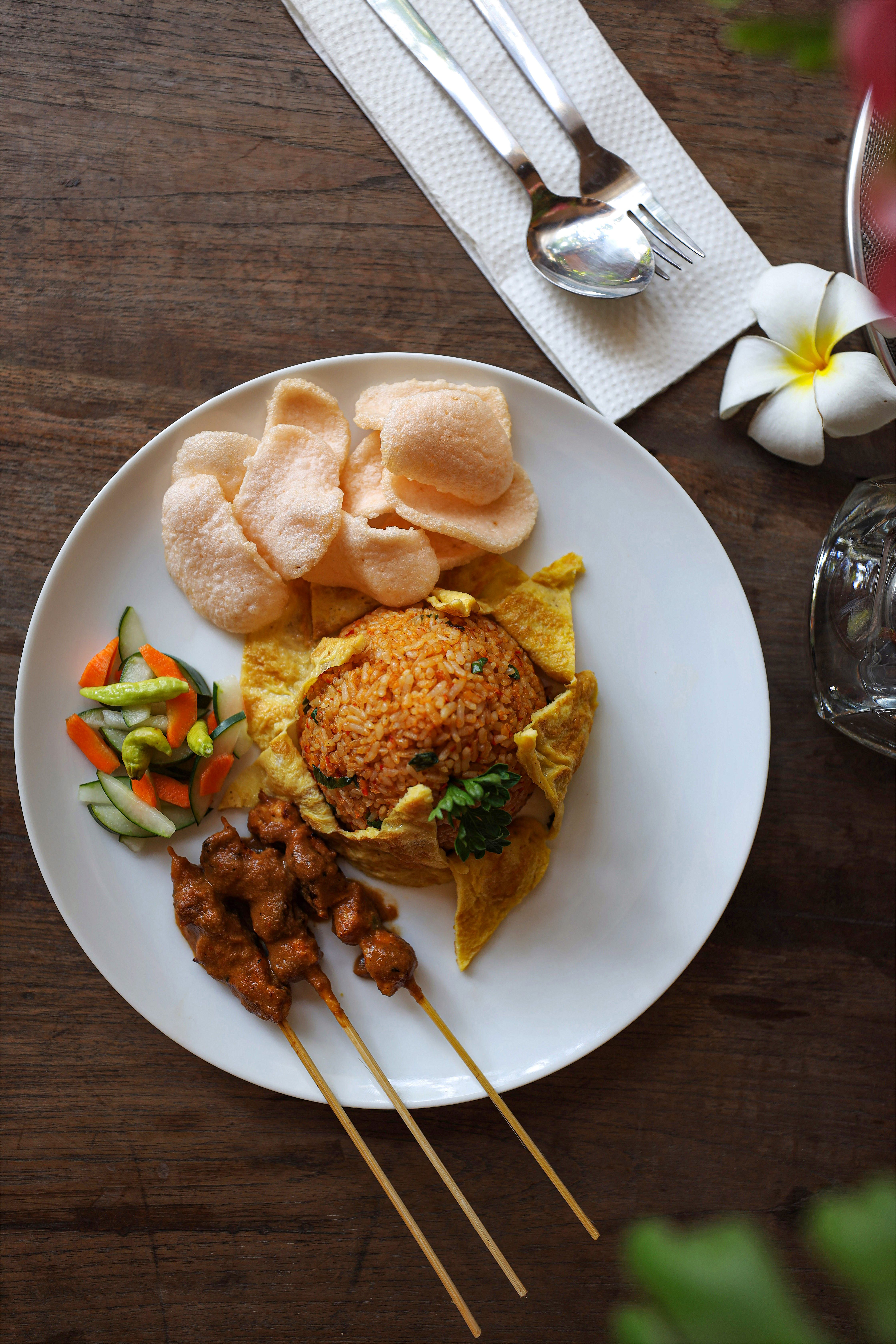 Assiette de riz sauté enveloppé d'omelette, avec brochettes satay et crackers de crevette