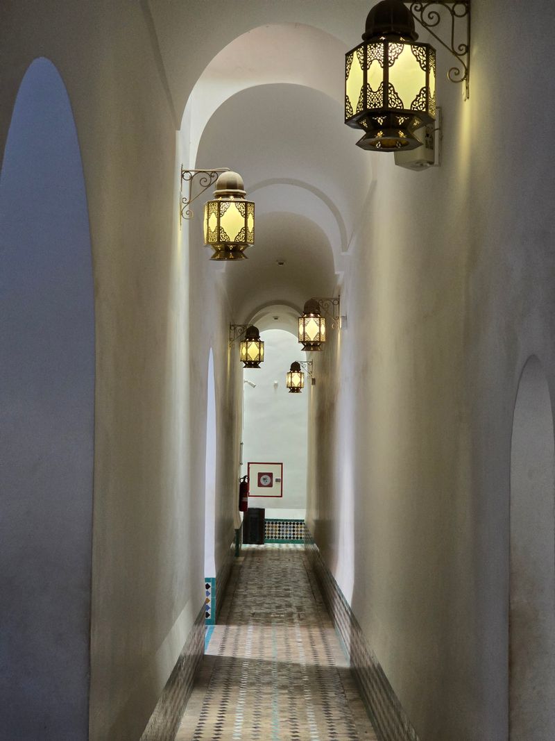 A white vaulted corridor lit by brass lanterns