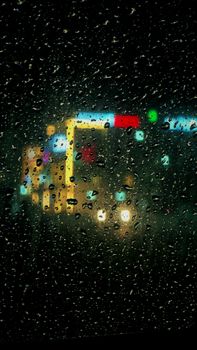 Raindrops on glass with colorful city lights blurred in the background.