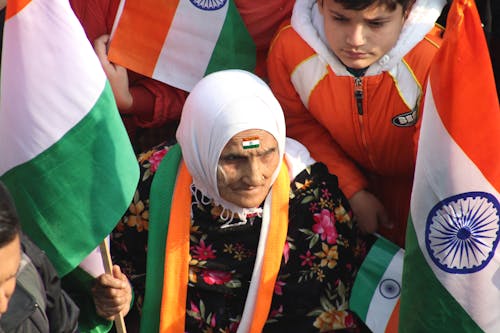 Gratis Seorang Wanita Lansia Duduk Bersama Sekelompok Orang Sambil Memegang Bendera Foto Stok