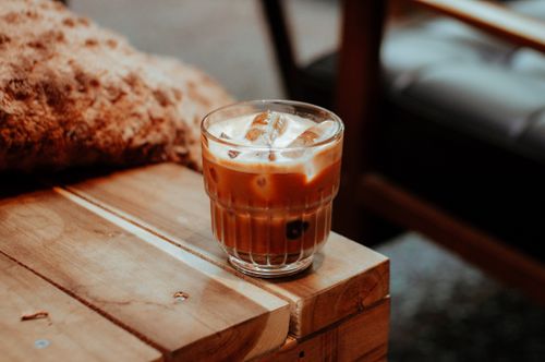 Free Glass of iced coffee with ice cubes on a textured wooden table, cozy cafe setting. Stock Photo