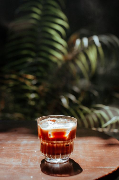 Free Iced coffee in a glass on a sunny wooden table, with fern shadows creating a tropical feel. Stock Photo