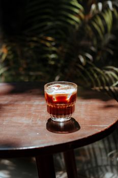 Glass of iced cold brew coffee sitting on a wooden table in sunlight.