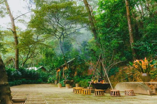 A serene outdoor forest setting featuring a cozy campfire, surrounded by lush greenery and rustic seating.
