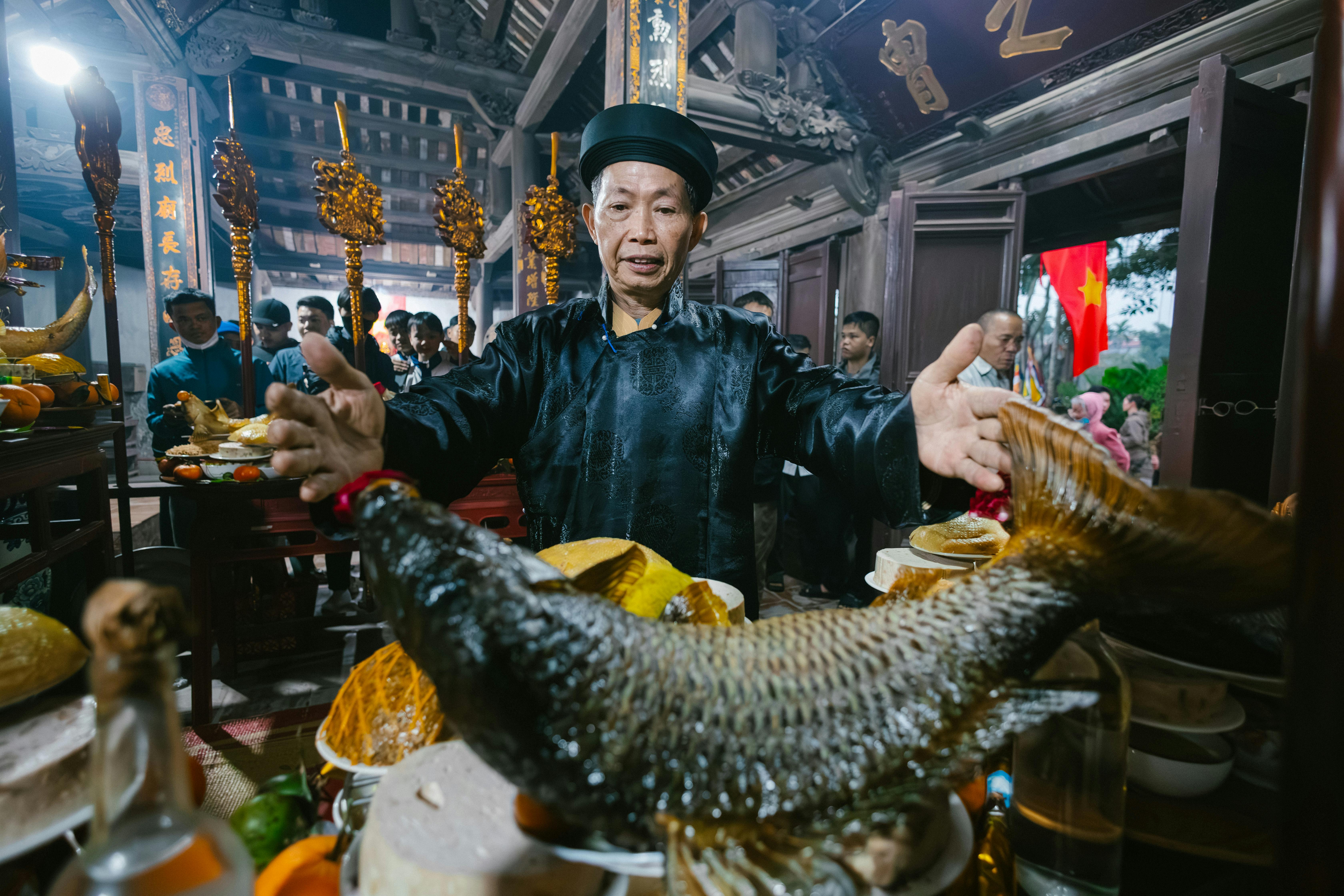 Kulturelle Zeremonie, bei der ein Mann eine große Fisch-Opfergabe in traditionellem Umfeld präsentiert.