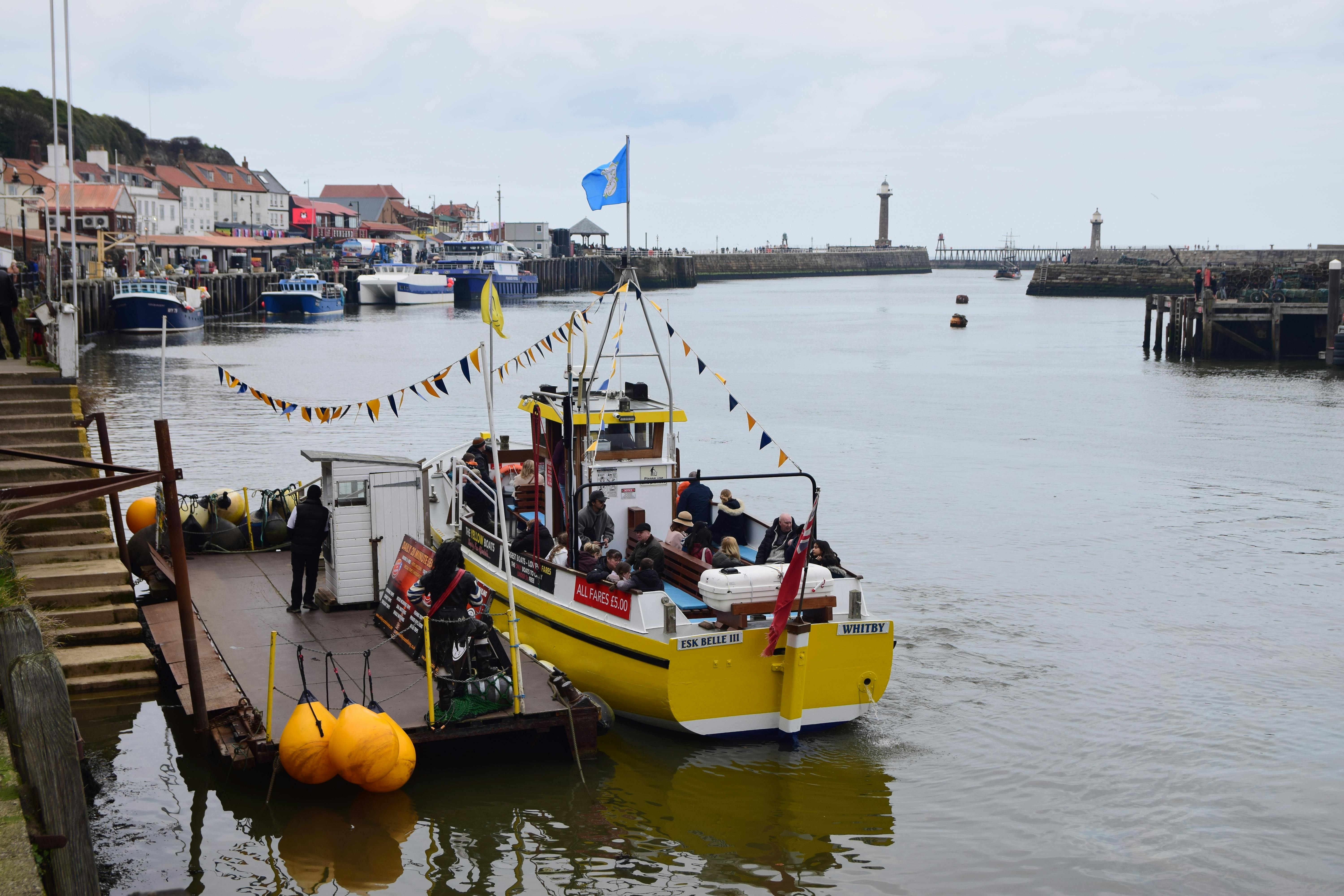 Fishing boat at Whitby Harbor, England, with people onboard and scenic waterfront views.