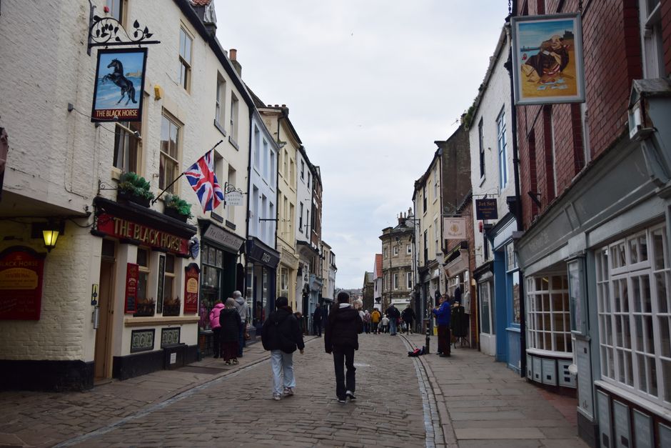 Cobblestone street lined with quaint shops and Union Jack flag in a historic English town.