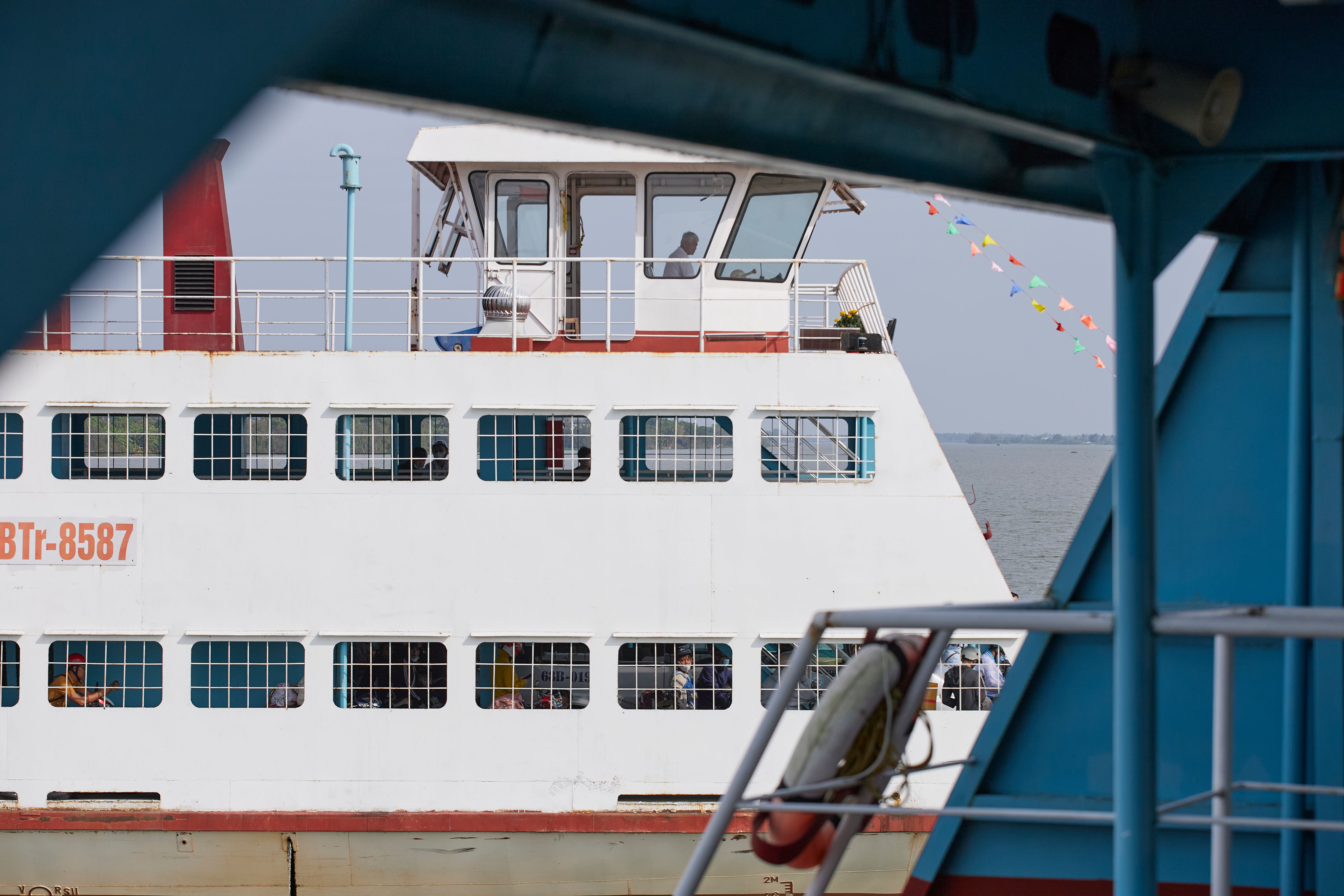 A passenger ferry boat crossing the river in An Hoi, Vinh Long, Vietnam, with colorful flags.