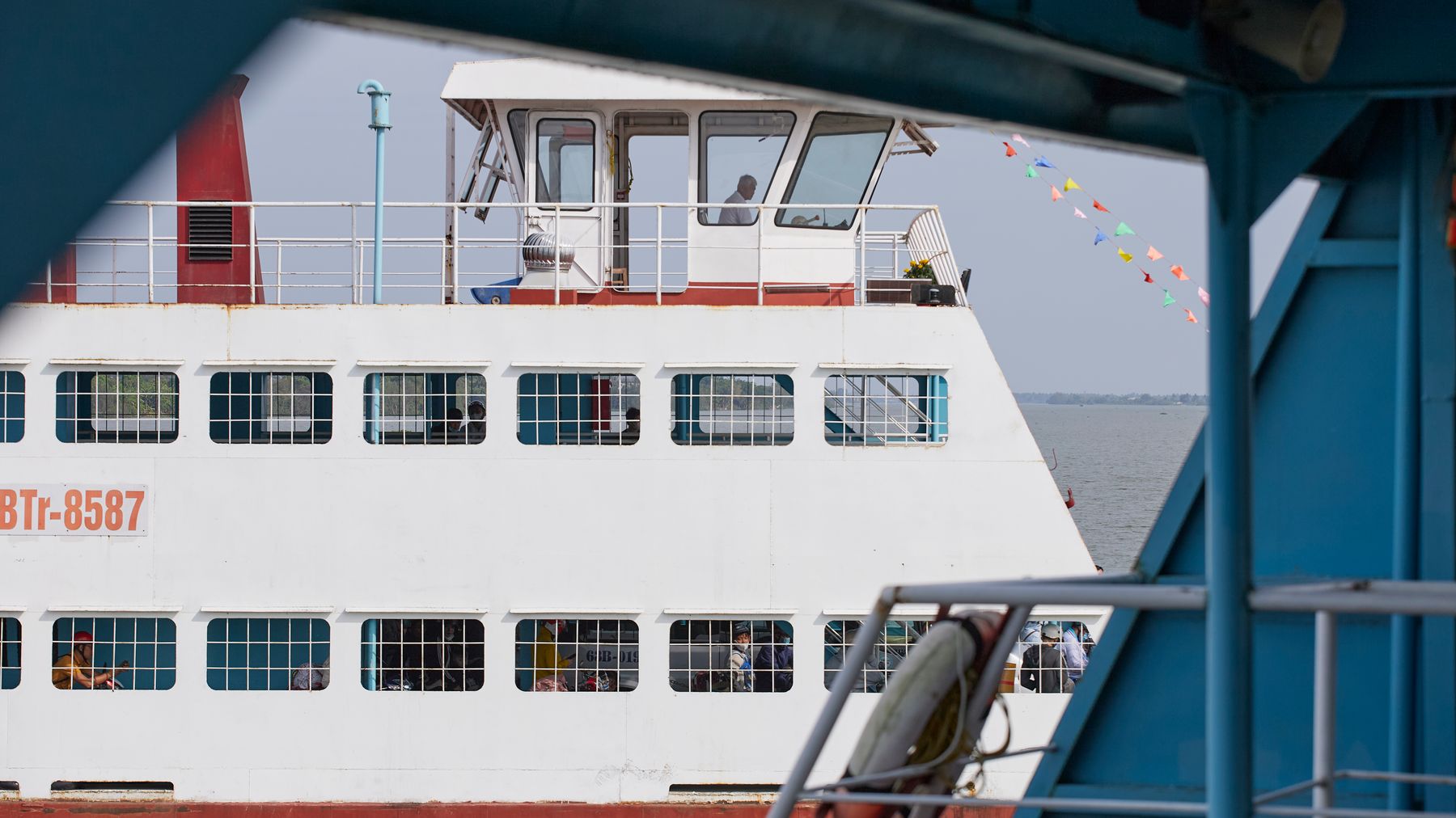 A passenger ferry boat crossing the river in An Hoi, Vinh Long, Vietnam, with colorful flags.
