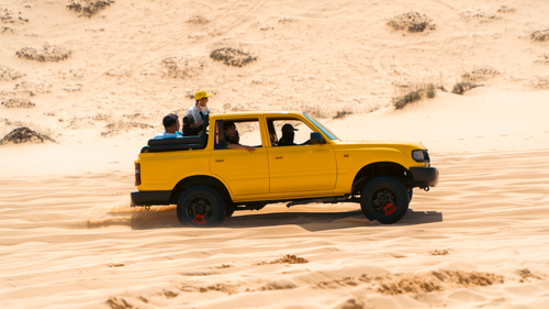 Free A yellow SUV with passengers drives through sandy desert dunes on a sunny day. Stock Photo