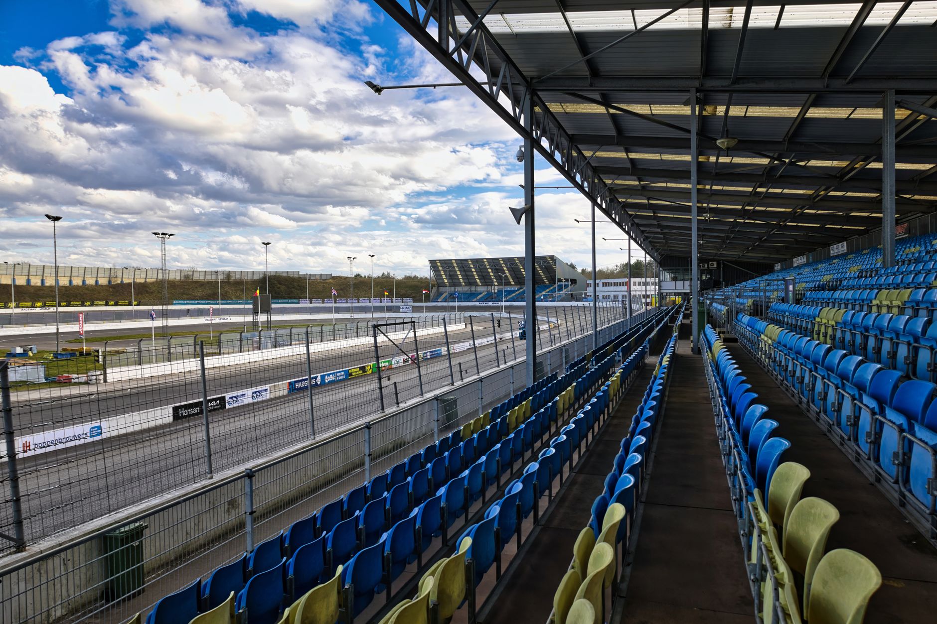 An expansive view of an empty grandstand at a motorsport track under a partly cloudy sky.