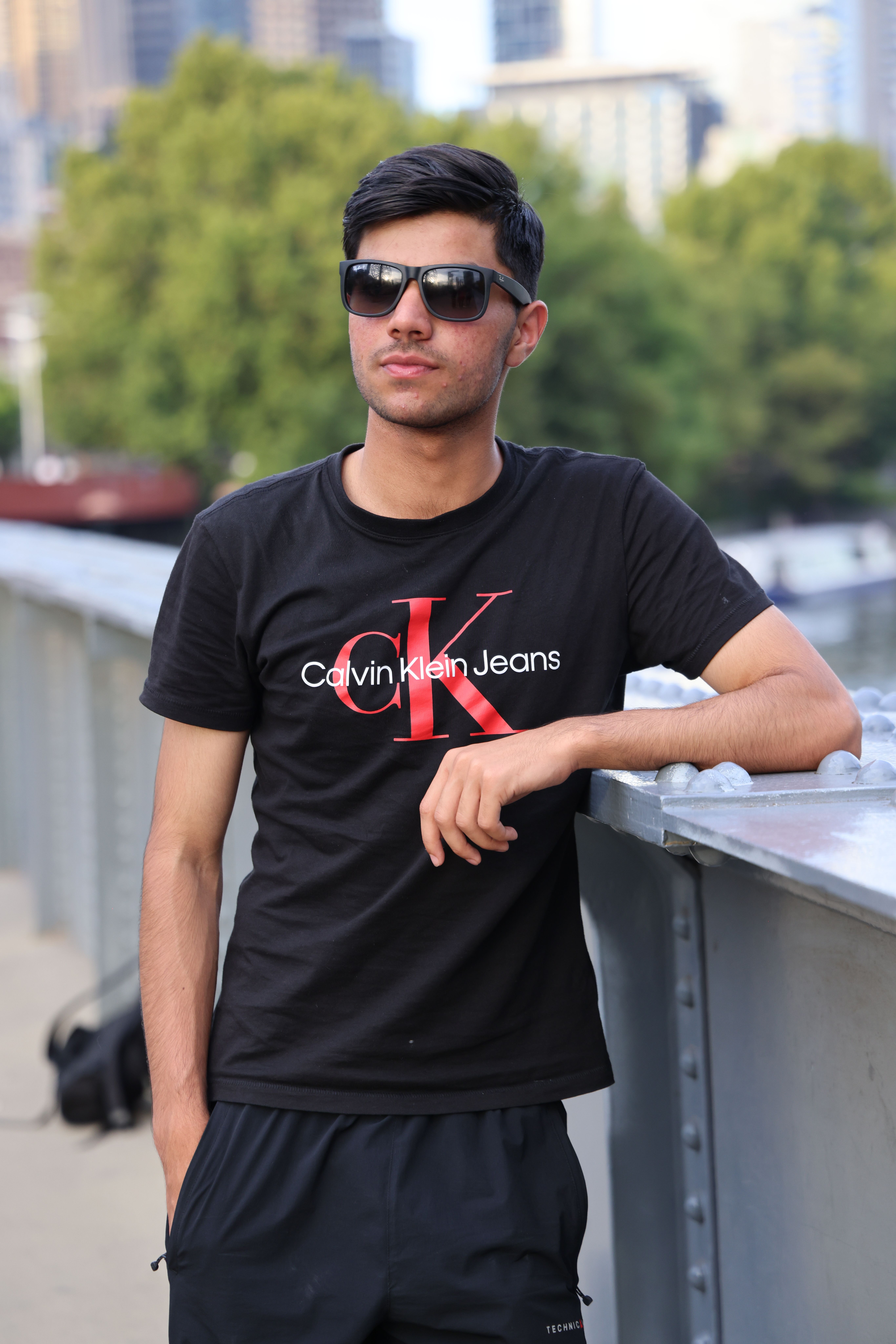 Young man wearing sunglasses and a Calvin Klein shirt, standing outdoors.