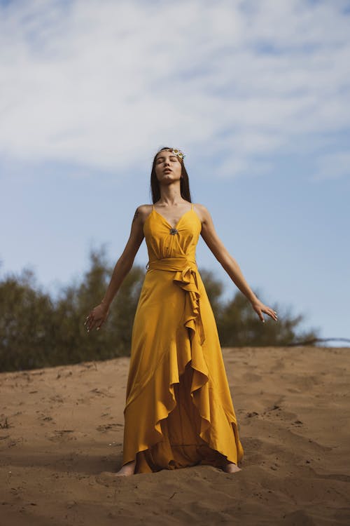 Woman in Yellow Dress Standing on Brown Sand