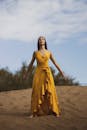 一个宁静的女人在蓝天下的沙丘上沉思着黄色的连衣裙