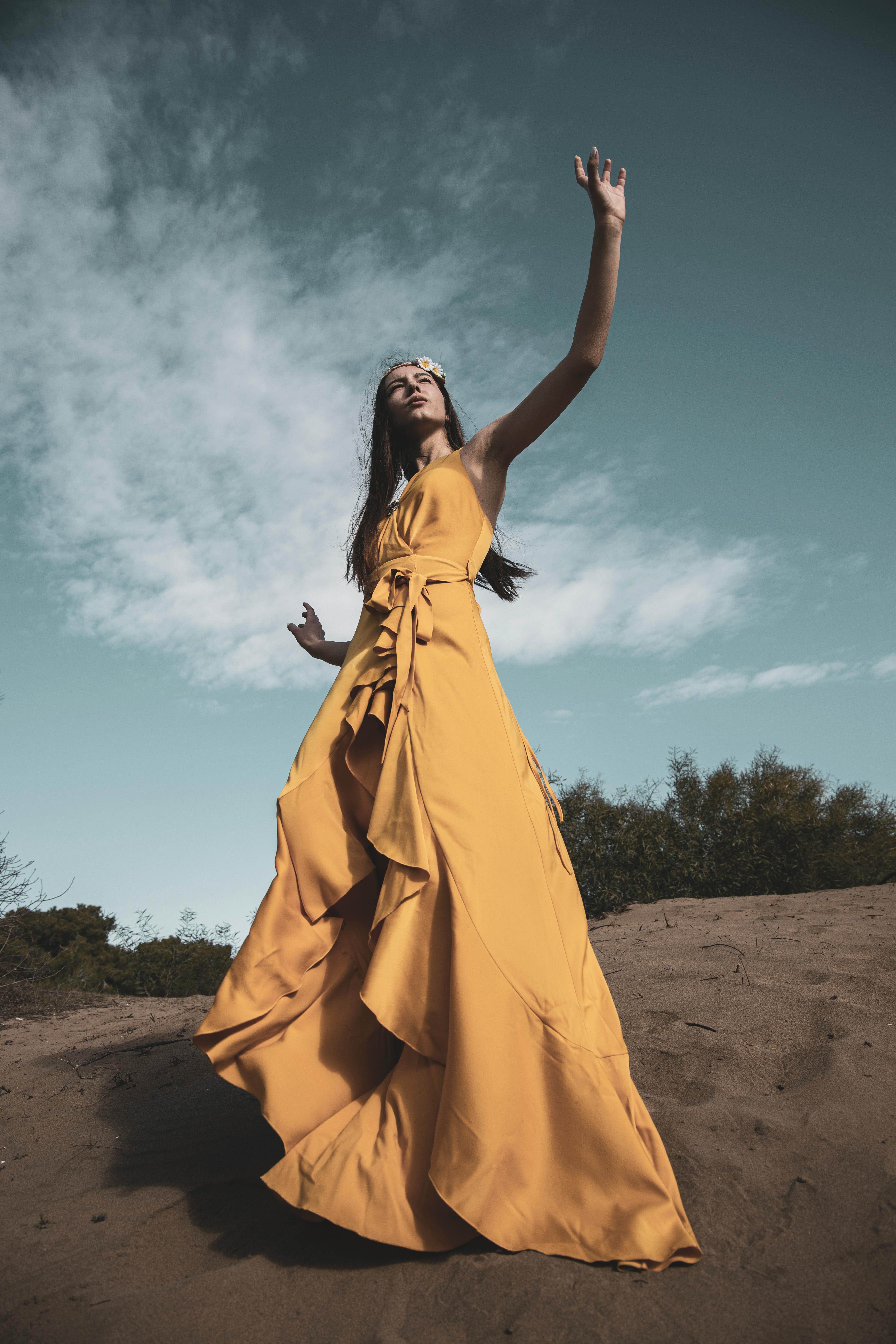 woman in yellow dress standing on brown sand under blue sky