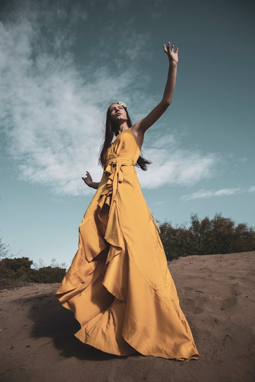Woman in Yellow Dress Standing on Brown Sand Under Blue Sky