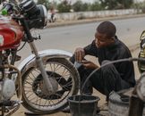 A young mechanic repairs a motorcycle tire on a road, showcasing hands-on mechanical skills.