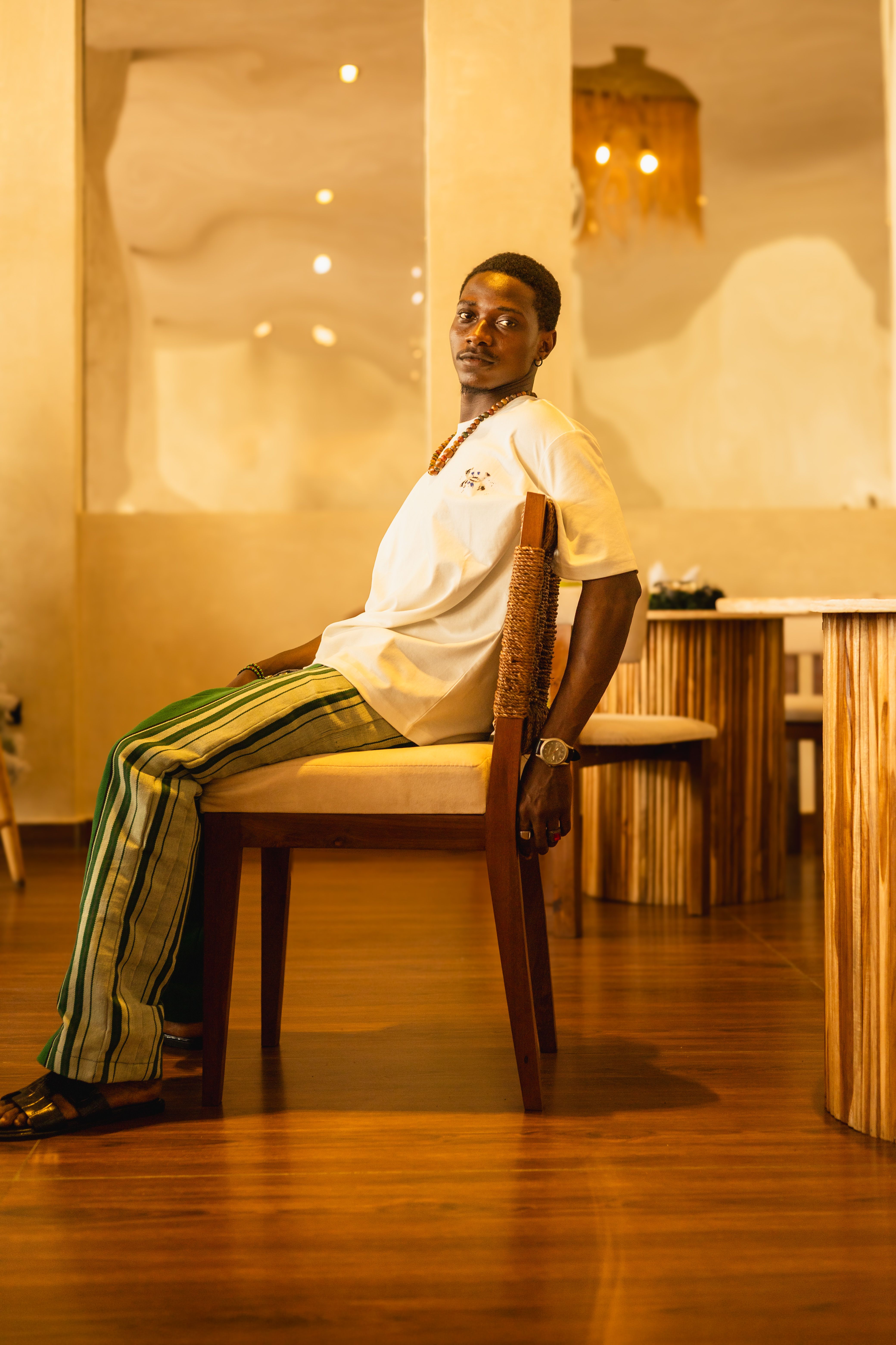 Stylish man in striped pants seated in contemporary Lagos cafe, showcasing African fashion.