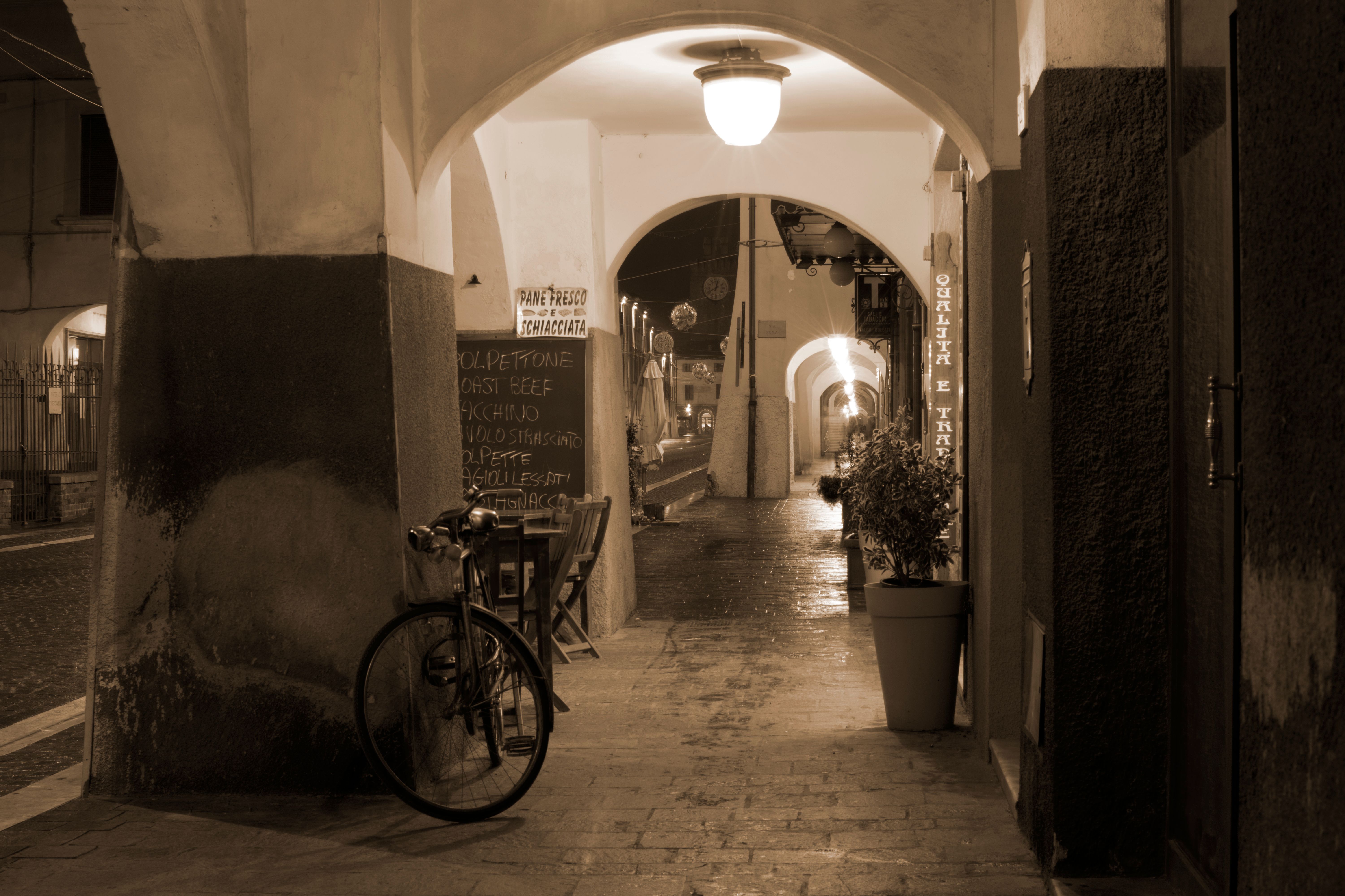 Rustic evening in a sepia-toned Cascina alleyway with warm lighting and a bicycle.