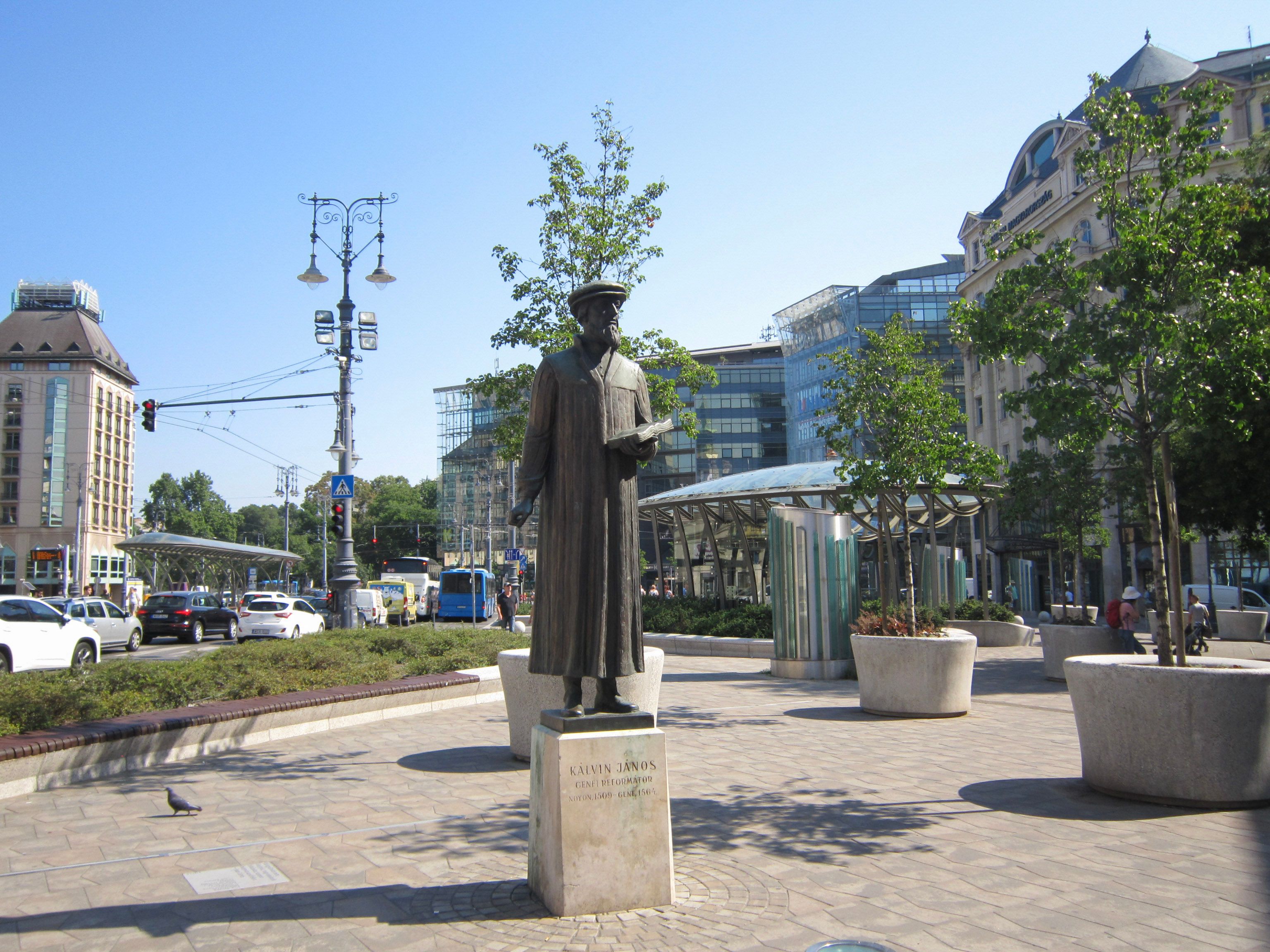Outdoor view of the Kálvin János statue amidst modern city architecture in Budapest, Hungary.