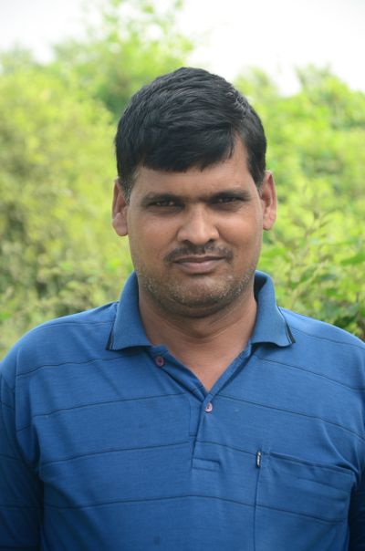 Casual portrait of an Indian man in a blue shirt with greenery in the background