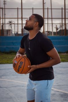 Adult man in sunglasses holding a basketball on an outdoor court during the day.