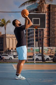 A man playing basketball on an outdoor court on a sunny day, aiming for the basket.