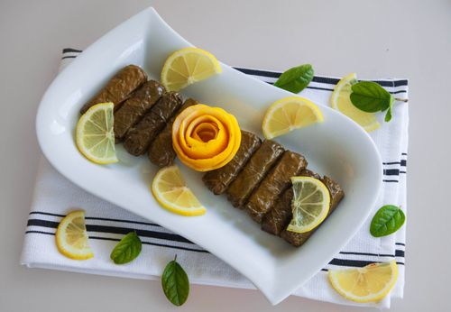 Free Delicious stuffed grape leaves decorated with sliced lemon and orange peel flower on a white plate. Stock Photo