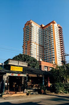 A modern skyscraper towers over a local diner in Chiang Mai, Thailand, under a clear blue sky.