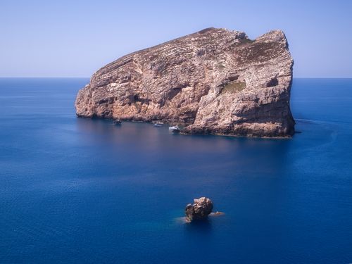 Free Stunning aerial photo of a rocky island surrounded by the clear blue sea in Sardinia, Italy, on a sunny day. Stock Photo