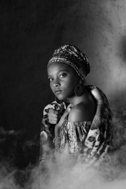 Black and white portrait of an elegant woman wearing a turban and floral outfit, enveloped in a smoky atmosphere.