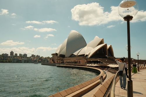 Free Scenic view of the Sydney Opera House with waterfront and tourists under sunny skies. Stock Photo
