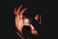 Crop person holding burning lightbulb in darkness