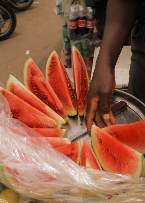 Free Vibrant watermelon slices displayed on a street vendor's tray, showcasing fresh and juicy summer fruits. Stock Photo